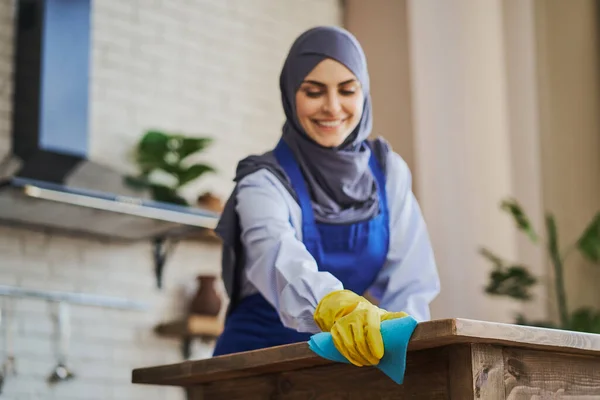 Arab nő, konyhaasztalt takarít, rongyot használ és kesztyűt visel. — Stock Fotó