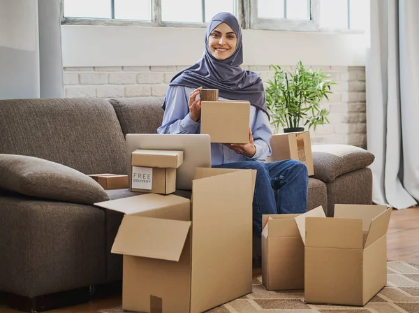 Araberin sitzt mit Laptop auf der Couch und packt Bestellungen ein — Stockfoto