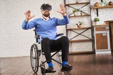 Tekerlekli sandalyede oturan ve VR kulaklık takan neşeli bir adam.