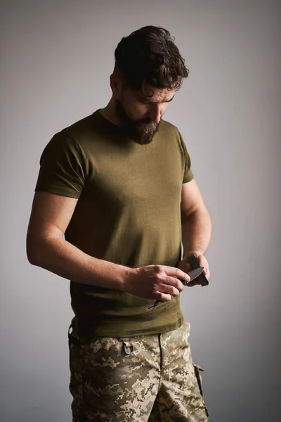 Strong military man sharpening his pocket knife with a whetstone