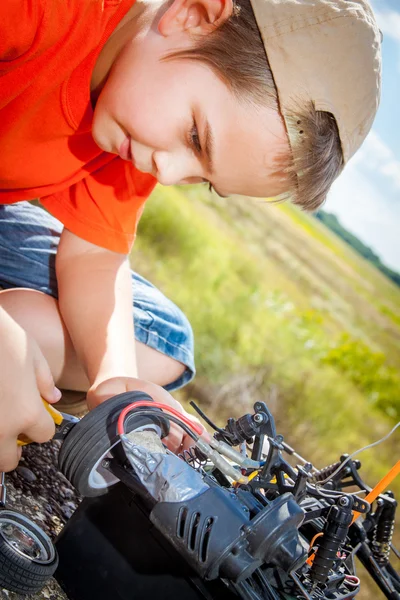 Kleiner Junge repariert Funkwagen in Feldnähe — Stockfoto