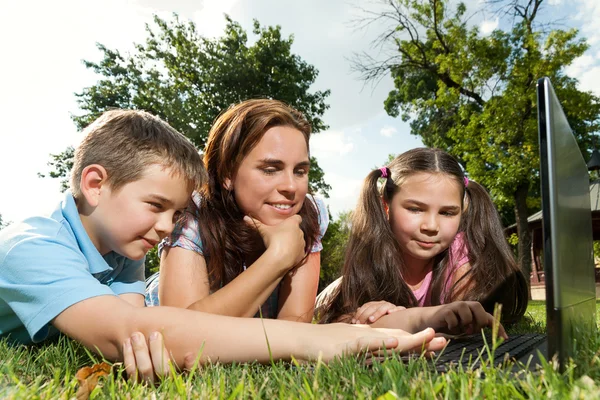 Mutlu bir aile çim üzerinde yalan dizüstü kullanarak — Stok fotoğraf