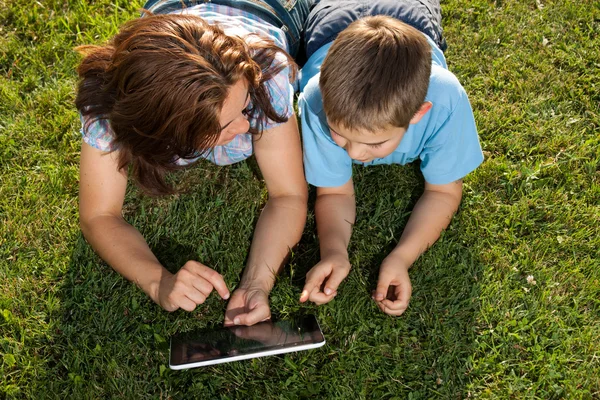 Lycklig familj använder laptop liggande på gräs — Stockfoto