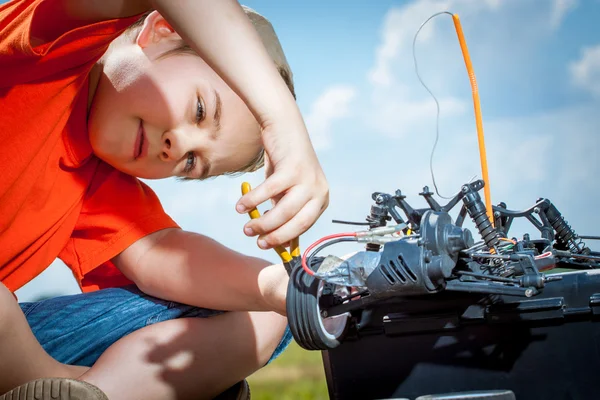 Мальчик ремонтирует радиоуправляемую машину на открытом воздухе возле поля. — стоковое фото