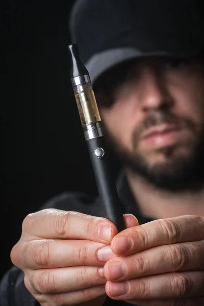 Jeune homme fumant cigarette électronique sur fond noir — Photo