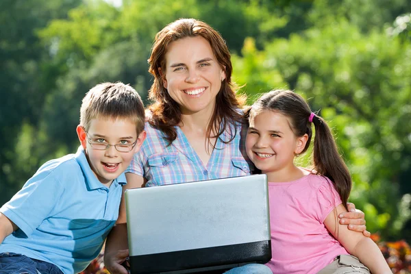 Familia feliz usando el ordenador portátil acostado en la hierba —  Fotos de Stock