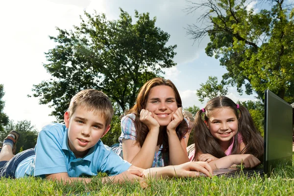 Famiglia felice utilizzando computer portatile sdraiato sull'erba — Foto Stock