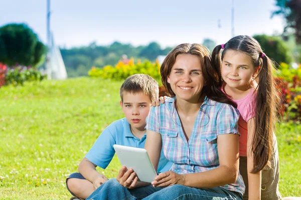 Glückliche Familie mit Laptop im Gras liegend — Stockfoto