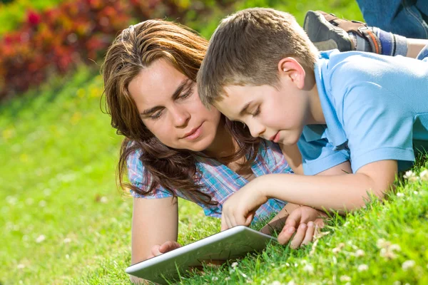 Met behulp van laptop liggen op gras en gelukkige familie — Stockfoto