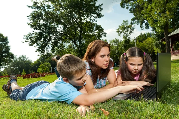 Familia feliz usando el ordenador portátil acostado en la hierba — Foto de Stock