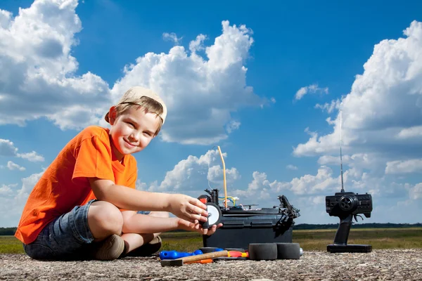 Pequeño chico reparar el coche de control de radio al aire libre cerca del campo — Foto de Stock