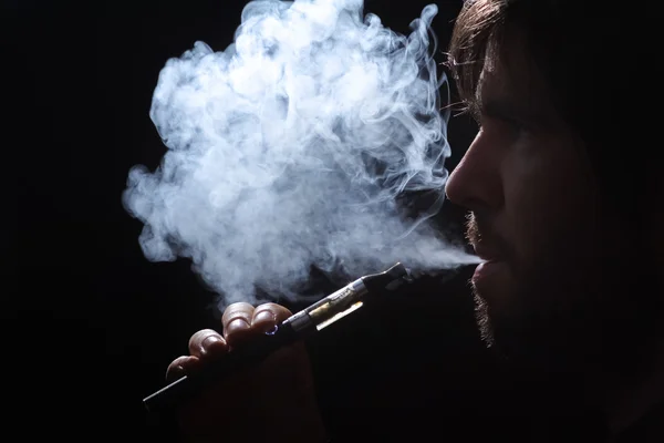 Hombre joven fumando cigarrillo electrónico sobre fondo negro — Foto de Stock