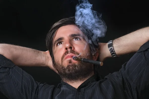 Hombre joven fumando cigarrillo electrónico sobre fondo negro — Foto de Stock