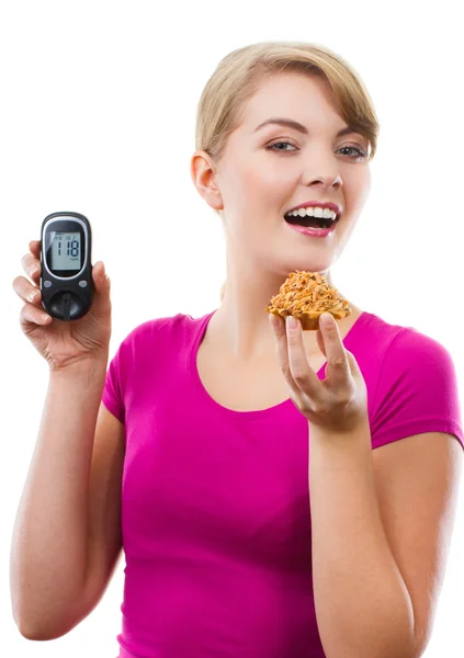 Mulher feliz segurando glicosímetro e comer cupcake fresco, medindo o nível de açúcar, conceito de diabetes — Fotografia de Stock