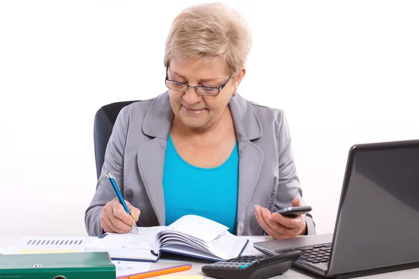 Пожилая деловая женщина, записывающая в блокнот и работающая за своим столом в офисе, бизнес-концепция — стоковое фото