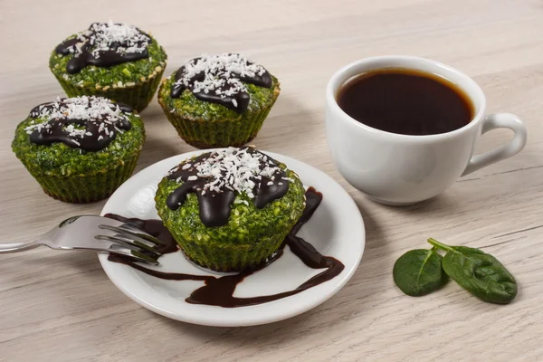 Frische Muffins mit Spinat, Kokosnuss, Schokoladenglasur und Tasse Kaffee, leckeres gesundes Dessert — Stockfoto