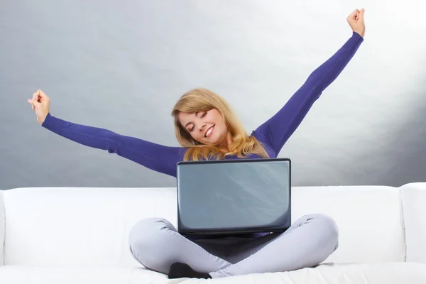 Happy woman with laptop sitting on sofa and stretching her hands — Zdjęcie stockowe