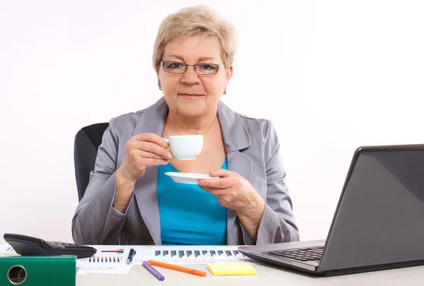 Anciana mujer de negocios que bebe té o café en el escritorio en la oficina, descanso en el trabajo — Foto de Stock