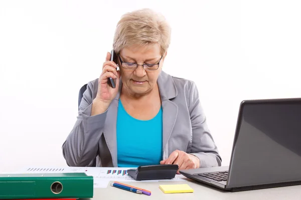 Idosa mulher de negócios falando no celular e trabalhando em sua mesa no escritório, conceito de negócio — Fotografia de Stock