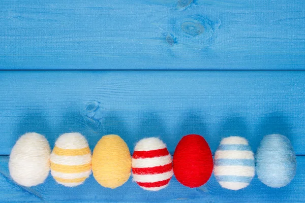 Easter eggs wrapped woolen string on blue wooden boards, copy space for text, decoration for Easter — Stock Photo, Image