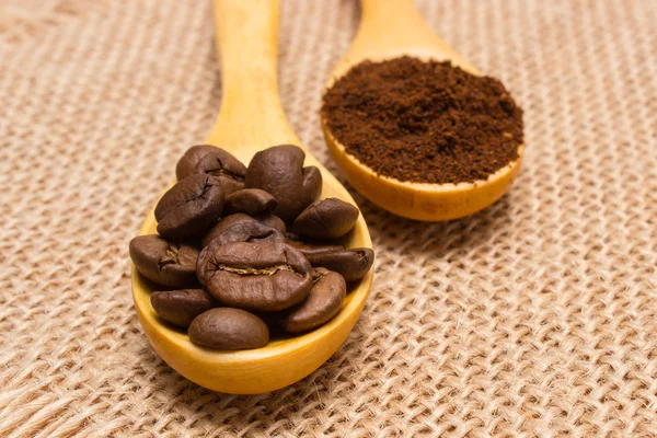 Grains and ground coffee with wooden spoon on jute canvas — Stock Photo, Image