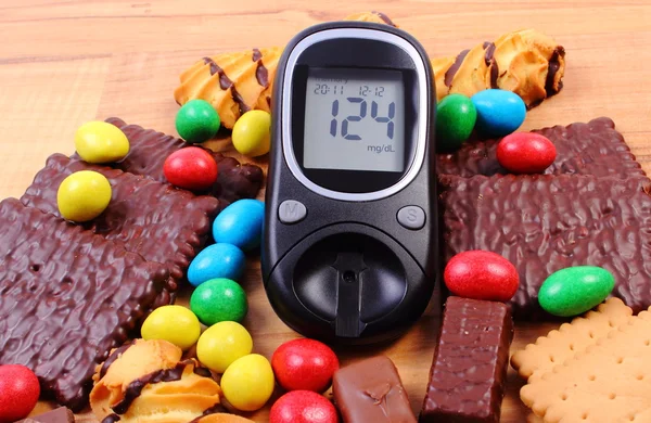 Glucometer con un montón de dulces en la superficie de madera, diabetes y alimentos poco saludables — Foto de Stock