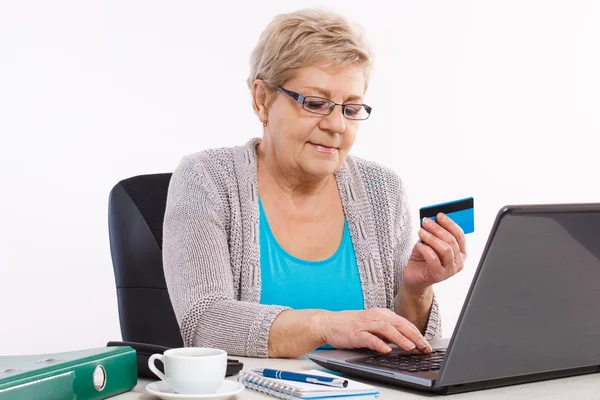 Пожилая женщина с кредитной картой и ноутбуком, оплачивающая коммунальные услуги или покупки в интернете — стоковое фото