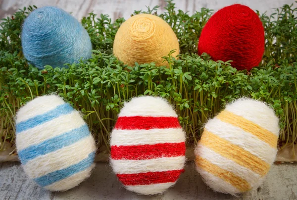 Huevos de Pascua envueltos en hilo de lana y berro verde sobre fondo de madera, decoración para Pascua —  Fotos de Stock