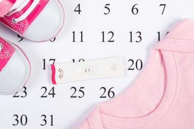 Pregnancy test with positive result and clothing for newborn on calendar, expecting for baby clipart
