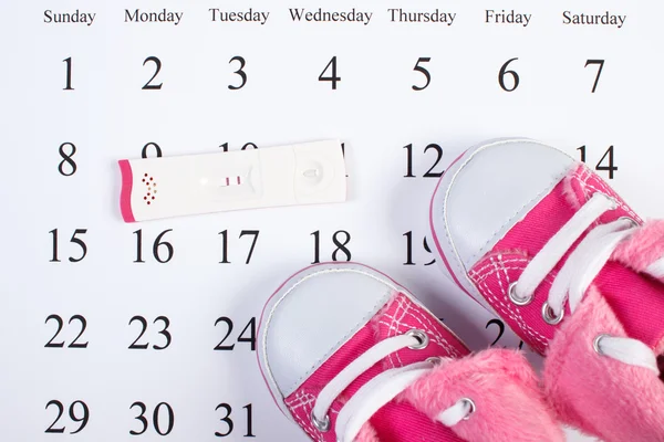 Test de grossesse avec résultat positif et chaussures de bébé sur le calendrier, attendant bébé — Photo
