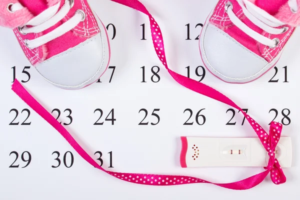 Pregnancy test with positive result and baby shoes on calendar, expecting for baby — Stock Photo, Image