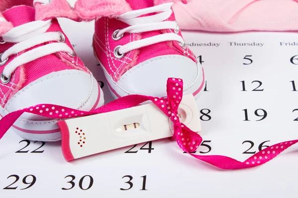 Schwangerschaftstest mit positivem Ergebnis und Babyschuhe auf dem Kalender, Baby erwartet — Stockfoto