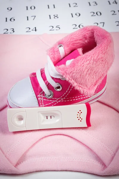 Teste de gravidez com resultado positivo e roupas para recém-nascido no calendário, esperando para o bebê — Fotografia de Stock