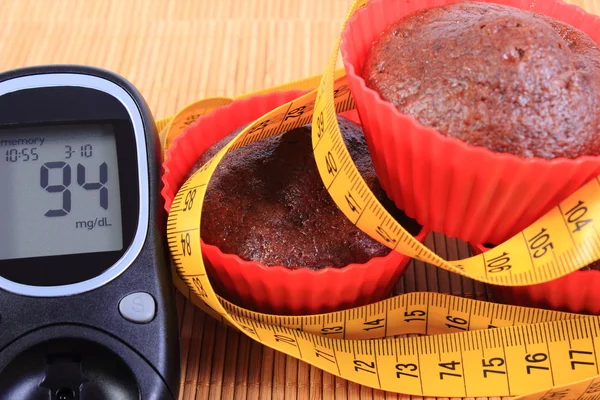 Glucomètre, muffins dans des tasses rouges et ruban à mesurer — Photo