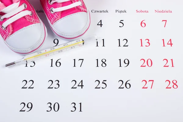 Thermometer und Schuhe für Neugeborene auf dem Kalender, Erwartung für Baby — Stockfoto