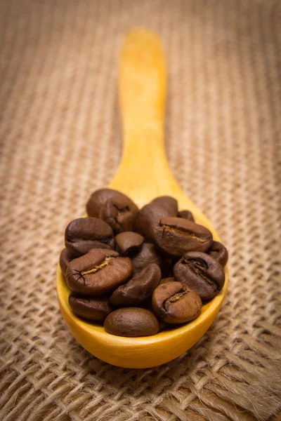 Haufen Kaffeebohnen mit Holzlöffel auf Jutescreme — Stockfoto