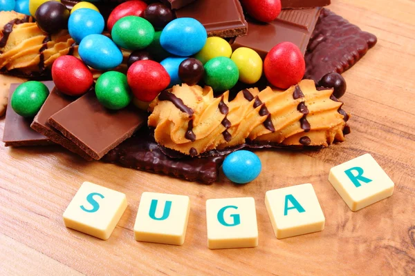 A lot of sweets with word sugar on wooden surface, unhealthy food — Stock Photo, Image