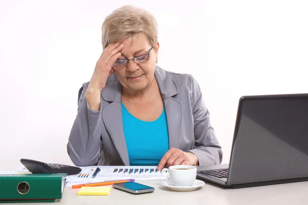 Пожилая деловая женщина, держащаяся за голову и работающая за столом в офисе, бизнес-концепция — стоковое фото