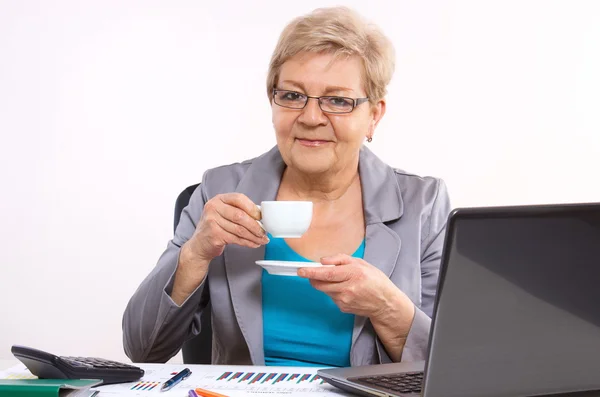 Ouderen zakenvrouw thee of koffie drinken bij balie in kantoor, pauze op het werk — Stockfoto