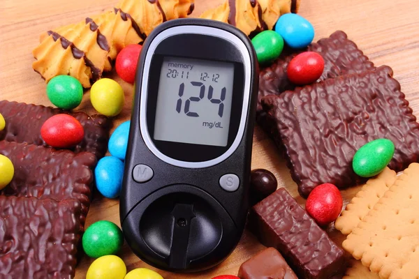 Glucometer with heap of sweets on wooden surface, diabetes and unhealthy food — Stock Photo, Image