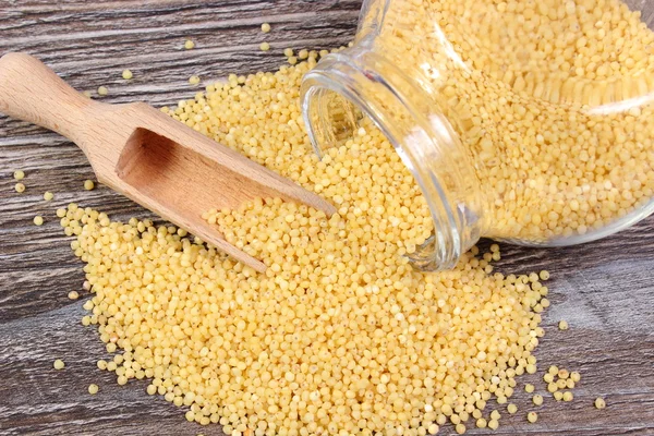 Millet groats spilling out of glass jar. Wooden background — Stock Photo, Image