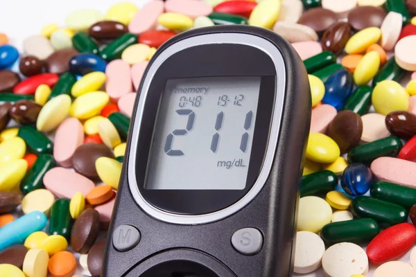 Glucometer with result sugar level and heap of medical pills and capsules, diabetes, health care concept