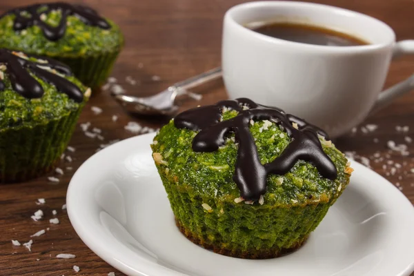 Frische Muffins mit Spinat, Kokosnuss, Schokoladenglasur und Tasse Kaffee, leckeres gesundes Dessert — Stockfoto