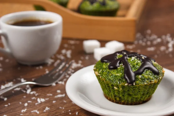 Frische Muffins mit Spinat, Kokosnuss, Schokoladenglasur und Tasse Kaffee, leckeres gesundes Dessert — Stockfoto
