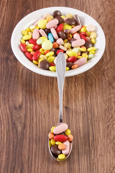 Medical pills on teaspoon and heap of colorful medical capsules on plate, health care concept — Stock Photo, Image