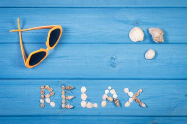 Word relax made of seashells, sunglasses on blue boards, summer time, copy space for text