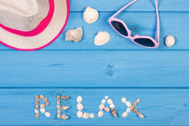 Word relax made of seashells, sunglasses and straw hat on blue boards, summer time, copy space for text