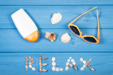 Word relax made of seashells, sunglasses and sun lotion on blue boards, summer time
