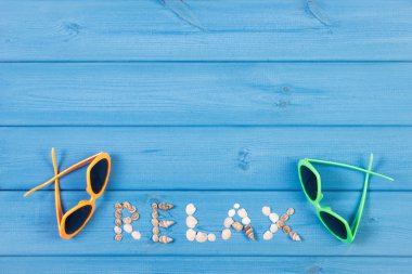 Word relax made of seashells, sunglasses on blue boards, summer time, copy space for text