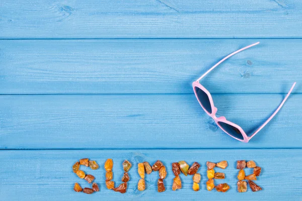 Palabra de verano hecha de piedras ámbar y gafas de sol en tablas azules, hora de verano, espacio de copia para el texto —  Fotos de Stock